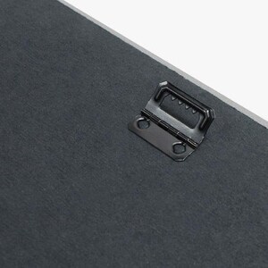 May include: Close-up of a black metal hanging hook attached to the back of a canvas painting.
