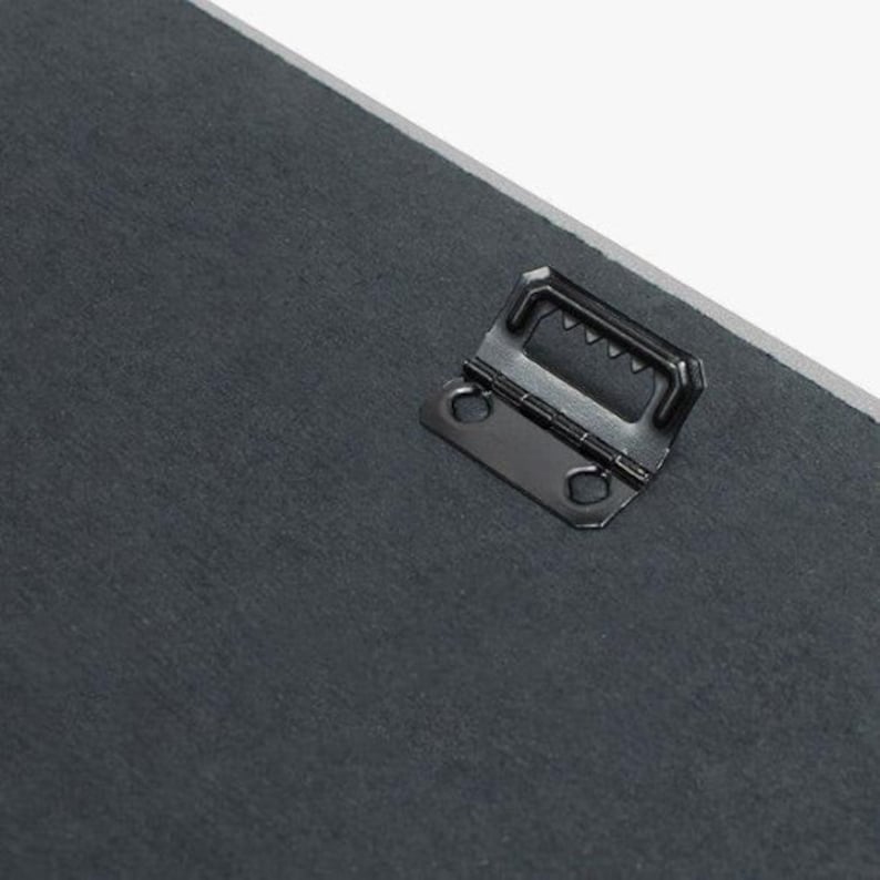May include: Close-up of a black metal hanging hook attached to the back of a canvas painting.