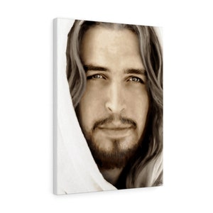 May include: A close-up portrait of a man with long brown hair and a beard. He is wearing a white robe and has a gentle expression on his face. His eyes are looking directly at the viewer.