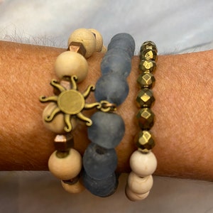 May include: A set of four bracelets featuring a sun charm, wooden beads, blue glass beads, and gold-toned beads.