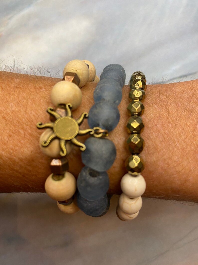 May include: A set of four bracelets featuring a sun charm, wooden beads, blue glass beads, and gold-toned beads.