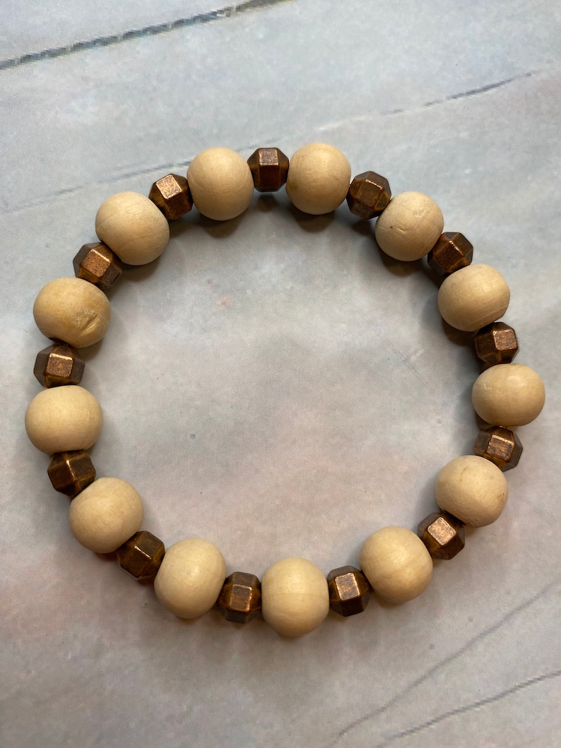 May include: A wooden bead bracelet with brown metal accents. The bracelet is made of natural wood beads and has a simple, elegant design.
