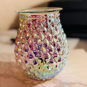 May include: Iridescent glass oil warmer with a textured, diamond-like pattern. The oil warmer has a clear glass dish at the top and is designed to hold scented oils. The colors shift from pink to blue and yellow.