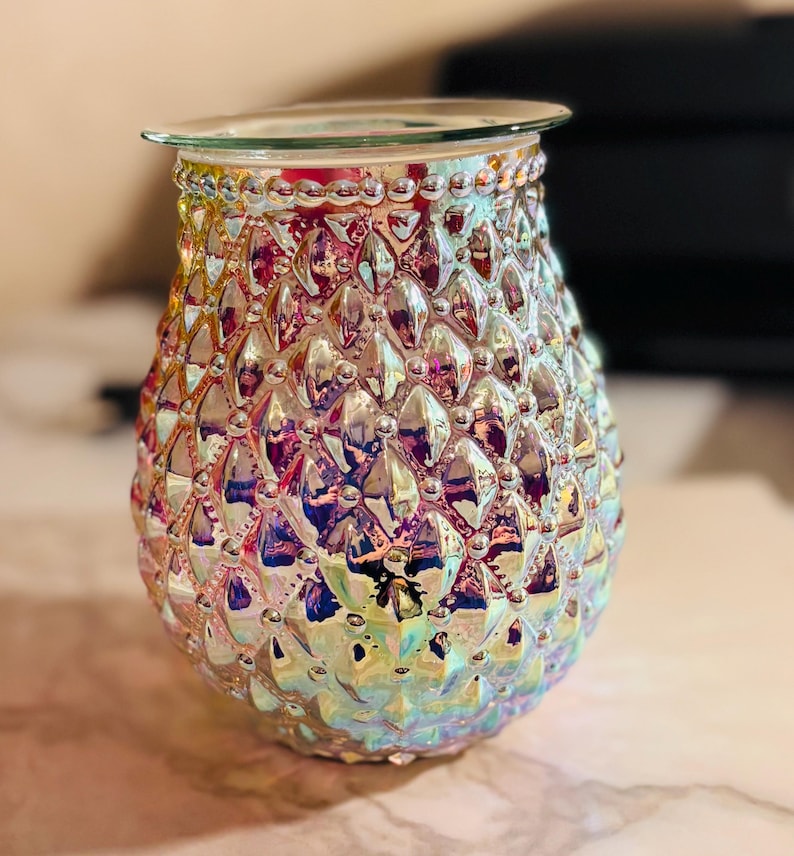May include: Iridescent glass oil warmer with a textured, diamond-like pattern. The oil warmer has a clear glass dish at the top and is designed to hold scented oils. The colors shift from pink to blue and yellow.
