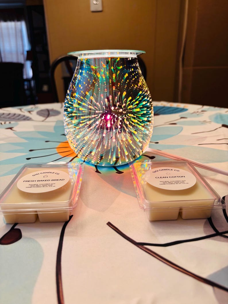 May include: A decorative glass wax warmer with a colorful firework design, with two wax melt containers. One container is labeled "Fresh Baked Bread" and the other is labeled "Clean Cotton".