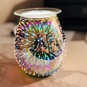 May include: A decorative glass oil warmer with a clear, round top and a bulbous body. The glass is iridescent, with a pattern of colorful, radiating dots in shades of pink, blue, yellow, and green. The warmer is designed to hold scented oils.