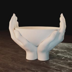 May include: A white ceramic bowl held by two sculpted hands. The hands are positioned as if cradling the bowl, with the fingers gently curved. The bowl and hands are a solid, matte white color.