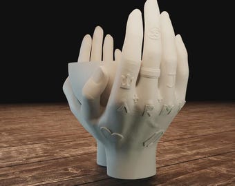 May include: A white ceramic hand-shaped planter with detailed tattoos and a ring. The planter is designed to hold small plants or decorative items. The fingers are slightly curved, creating a unique and artistic display piece.