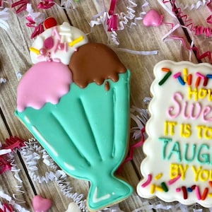 May include: Two decorated sugar cookies. One cookie is shaped like an ice cream cone with pink, brown, and white icing. The other cookie is rectangular with white icing and the text "How Sweet It Is To Be Taught By You" in colorful icing.