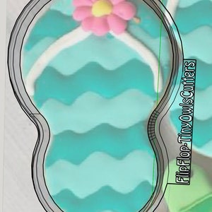 Puede incluir: Un cortador de galletas de chancla azul turquesa con un contorno blanco y una flor rosa en la parte superior. El cortador de galletas está hecho de metal y tiene un patrón ondulado en la suela. El texto "Flip-Flop Tiny Owl Cutters" es visible en el fondo.