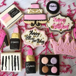 Puede incluir: Un conjunto de 10 galletas de azúcar decoradas con un tema rosa y dorado. Las galletas tienen forma de lápiz labial, zapato de tacón alto, paleta de maquillaje, botella de esmalte de uñas, pastel, corona y dos letreros que dicen "Feliz cumpleaños número 18".