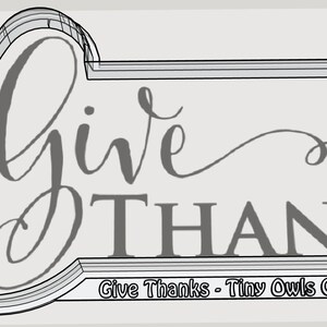 May include: A gray cookie cutter in the shape of a sign with the words "Give Thanks" in a script font. A sprig of leaves and berries is on the left. The text "Give Thanks - Tiny Owls Cutters" is at the bottom.