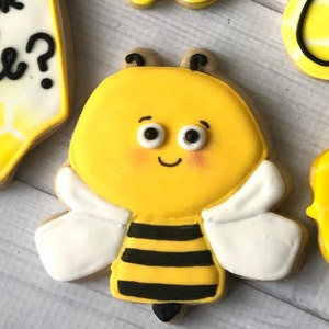 May include: A yellow and black bee cookie with white wings. The bee has a smiling face with big eyes and rosy cheeks.