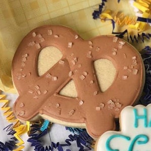 Puede incluir: Una galleta de azúcar moreno con forma de pretzel con cristales de sal en la parte superior. La galleta está sobre un fondo amarillo y azul.