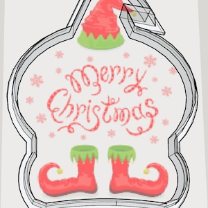 May include: A Christmas-themed cookie cutter in the shape of an elf. The design features a red elf hat and boots, green accents, and the words "Merry Christmas" in red script. Pink snowflakes are scattered around the text.