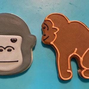 May include: Two decorated sugar cookies shaped like gorillas. One cookie is gray with a white face and black eyes. The other cookie is brown with a light brown outline.