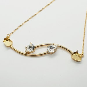 May include: A gold necklace with a delicate chain and a curved bar with three clear crystal stones.