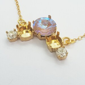 May include: A gold necklace with a pendant featuring three round settings for stones. The center setting has a large iridescent stone, while the two smaller settings have clear stones.