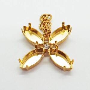 May include: Gold-tone metal pendant with a flower design featuring four oval-shaped settings and a small clear rhinestone in the center. The pendant has a chain attached to the top.