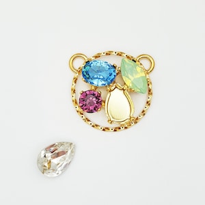 May include: A gold pendant with a circular design featuring a variety of colorful rhinestones. The pendant is surrounded by a twisted gold wire. A single clear rhinestone is also shown.