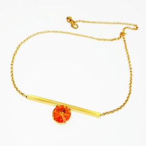 May include: A gold chain necklace with a thin gold bar and a large orange crystal pendant.