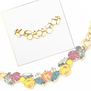 May include: A gold chain necklace with colorful gemstone accents. The necklace features a variety of shapes and sizes of gemstones, including round, oval, and marquise. The gemstones are set in gold settings and are arranged in a random pattern. The necklace is a statement piece that would be perfect for a special occasion.