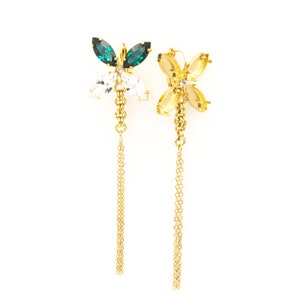 Puede incluir: Un par de pendientes de oro con diseño de mariposa. Cada pendiente presenta una mariposa de cristal verde y blanco con una cadena de oro colgante.