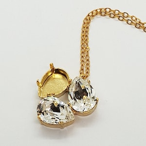 May include: A gold chain necklace with three pear-shaped crystal pendants. The pendants are clear and have a faceted design.