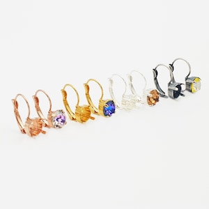 May include: A set of six pairs of gold, silver, and black earring settings with different colored crystals. The crystals are purple, blue, clear, amber, and yellow.