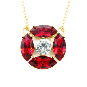 May include: A gold chain necklace with a pendant featuring a large clear rhinestone surrounded by four red marquise-shaped rhinestones.