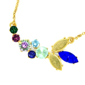May include: A gold chain necklace with a variety of colorful gemstones, including green, purple, pink, blue, and light blue. The necklace features two gold leaf-shaped pendants.