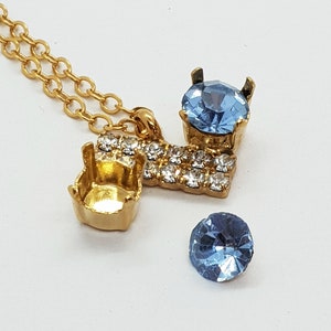 May include: A gold necklace with a pendant featuring a blue rhinestone and a row of smaller rhinestones. The pendant is attached to a gold chain with a lobster clasp.