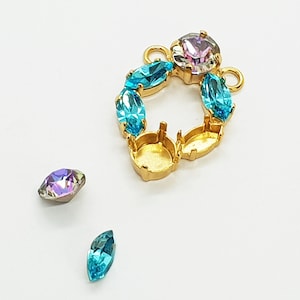 May include: Gold-tone metal setting with a round center and a ring of prong settings. The setting is decorated with blue and purple rhinestones. There are two loose rhinestones, one blue and one purple, next to the setting.
