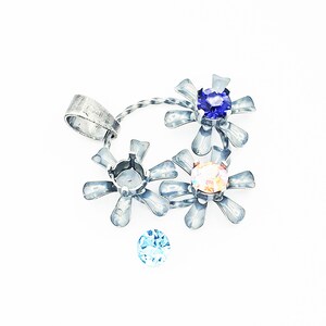 May include: Silver pendant with three flower-shaped charms, each with a different colored gemstone. The gemstones are blue, pink, and light blue.