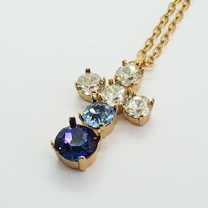 May include: A gold necklace with a cross pendant featuring five clear and blue gemstones. The center stone is a large, oval-shaped, dark blue gemstone.