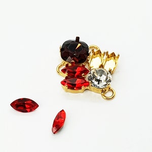 May include: Assortment of red, clear, and dark red rhinestones with gold settings. The rhinestones are in various shapes, including oval and marquise.