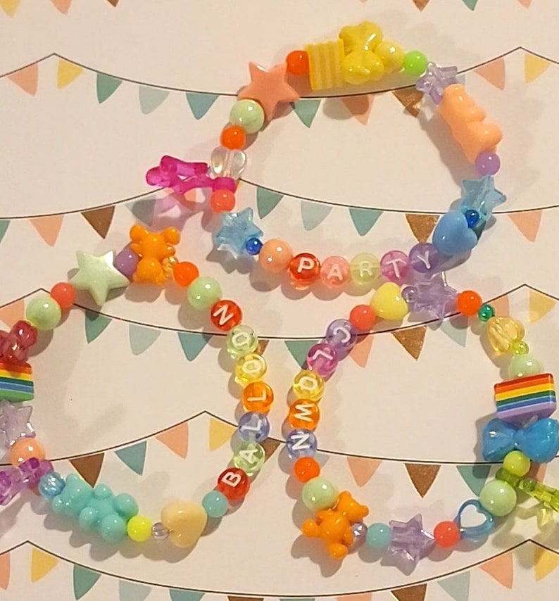 Pu&ograve; includere: Tre braccialetti colorati con perline e ciondoli arcobaleno, stelle e cuori. I braccialetti compongono le parole "BALLOON", "PARTY" e "NUMBERS".