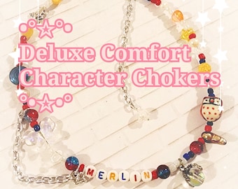 May include: A colorful beaded choker necklace with a silver chain and charms. The beads are red, white, blue, yellow, and orange. The charms include a small owl, a heart, and a star. The necklace spells out "MERLIN" in colorful letter beads.