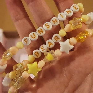 Pu&ograve; includere: Tre braccialetti di perline con perline gialle e bianche e ciondoli a forma di stella. I braccialetti compongono le parole "FUNSHINE", "BEAR" e "INE".