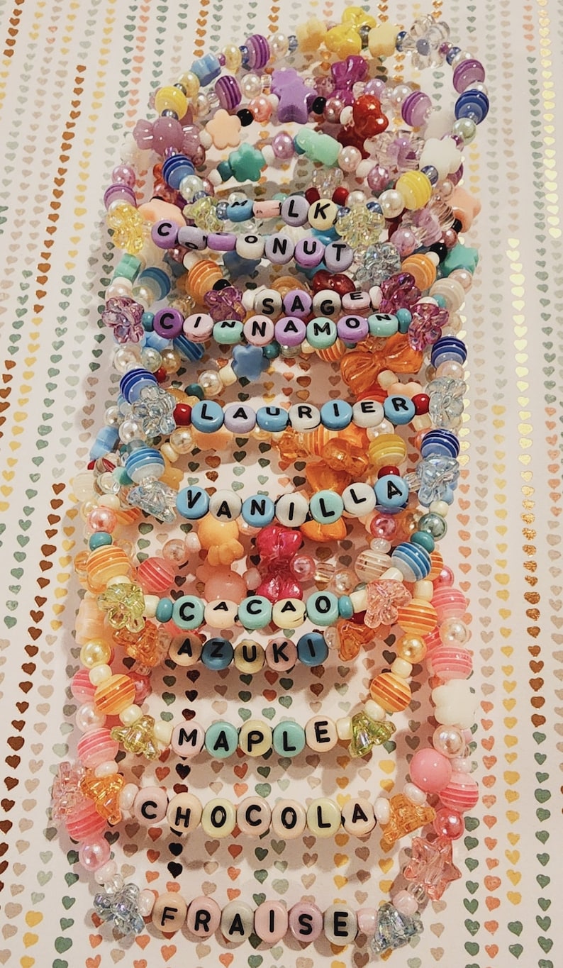 Pu&ograve; includere: Un mucchio di braccialetti colorati con perline, con diversi nomi scritti su di essi, tra cui "LK", "Coconut", "Sage", "Cinnamon", "Laurier", "Vanilla", "Cacao", "Azuki", "Maple", "Chocola" e "Fraise".