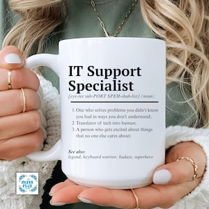 Puede incluir: Taza de cerámica blanca con el texto "IT Support Specialist" y una definición. La definición incluye tres puntos sobre el rol. El texto adicional incluye "Ver también: legend; keyboard warrior; badass; superhero".