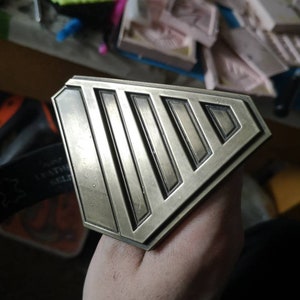 May include: A gold-toned metal ring with a geometric design featuring five parallel lines. The ring is worn on a person's finger.