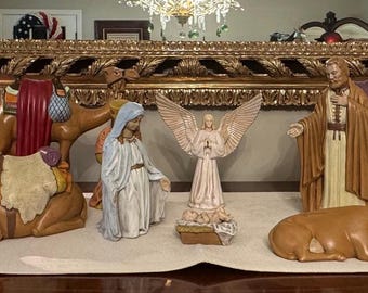 May include: A nativity scene with multiple figurines, including the three wise men, an angel, Mary, Joseph, and animals. The figurines are painted in various colors, with gold accents, and are arranged on a white tablecloth.