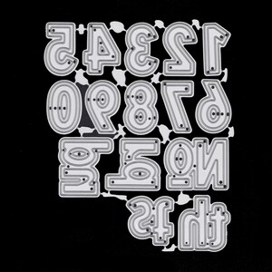 May include: A die-cut set of numbers in a bold, rounded font. The numbers 0 through 9 are visible, along with the numbers 1 and 2 in a mirrored orientation. The die-cut is made of silver metal and is set against a black background.