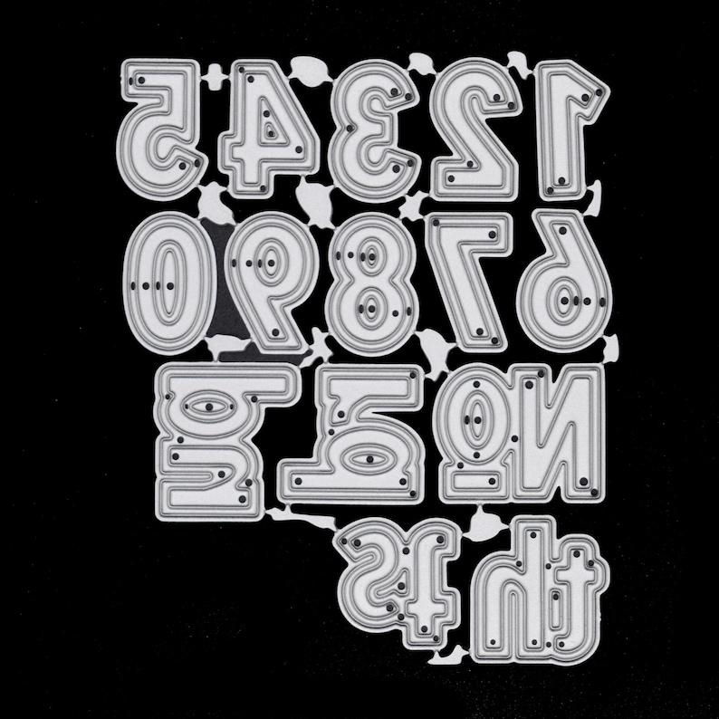 May include: A die-cut set of numbers in a bold, rounded font. The numbers 0 through 9 are visible, along with the numbers 1 and 2 in a mirrored orientation. The die-cut is made of silver metal and is set against a black background.