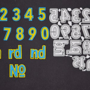 May include: A collection of number and ordinal die cuts in blue and yellow, and silver metal. The numbers 1 through 0 are in a bold, rounded font with a blue outline and yellow fill. Ordinal abbreviations are also included.