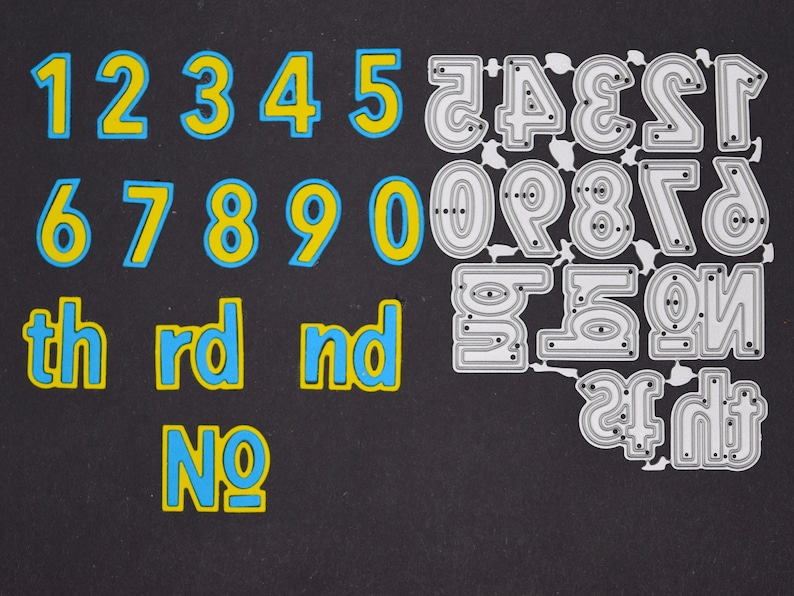 May include: A collection of number and ordinal die cuts in blue and yellow, and silver metal. The numbers 1 through 0 are in a bold, rounded font with a blue outline and yellow fill. Ordinal abbreviations are also included.