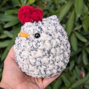 May include: A white and black crocheted chicken plush toy with a red pom-pom on its head. The chicken has a yellow beak and black eyes.