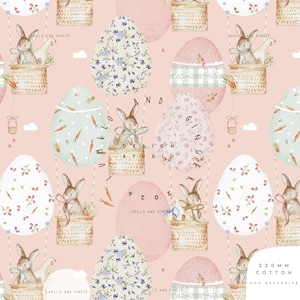 Può includere: Un motivo ripetuto con uova di Pasqua e coniglietti in mongolfiera. Le uova sono decorate con motivi floreali e di carote. I coniglietti sono in cesti di vimini. Lo sfondo è rosa tenue. I testi "LUMELO AND GINGER" e "220 MM COTTON NON EXCLUSIVE" sono visibili.