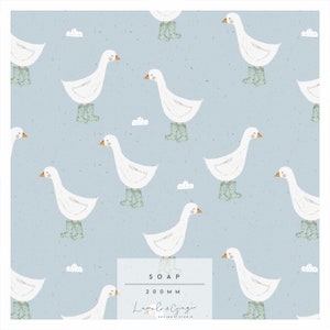 Pode incluir: Um padrão sem costura com gansos brancos usando botas de chuva verdes em um fundo azul claro com nuvens brancas. O padrão é intitulado "SOAP 200MM Lumila & Ginger DESIGN STUDIO".